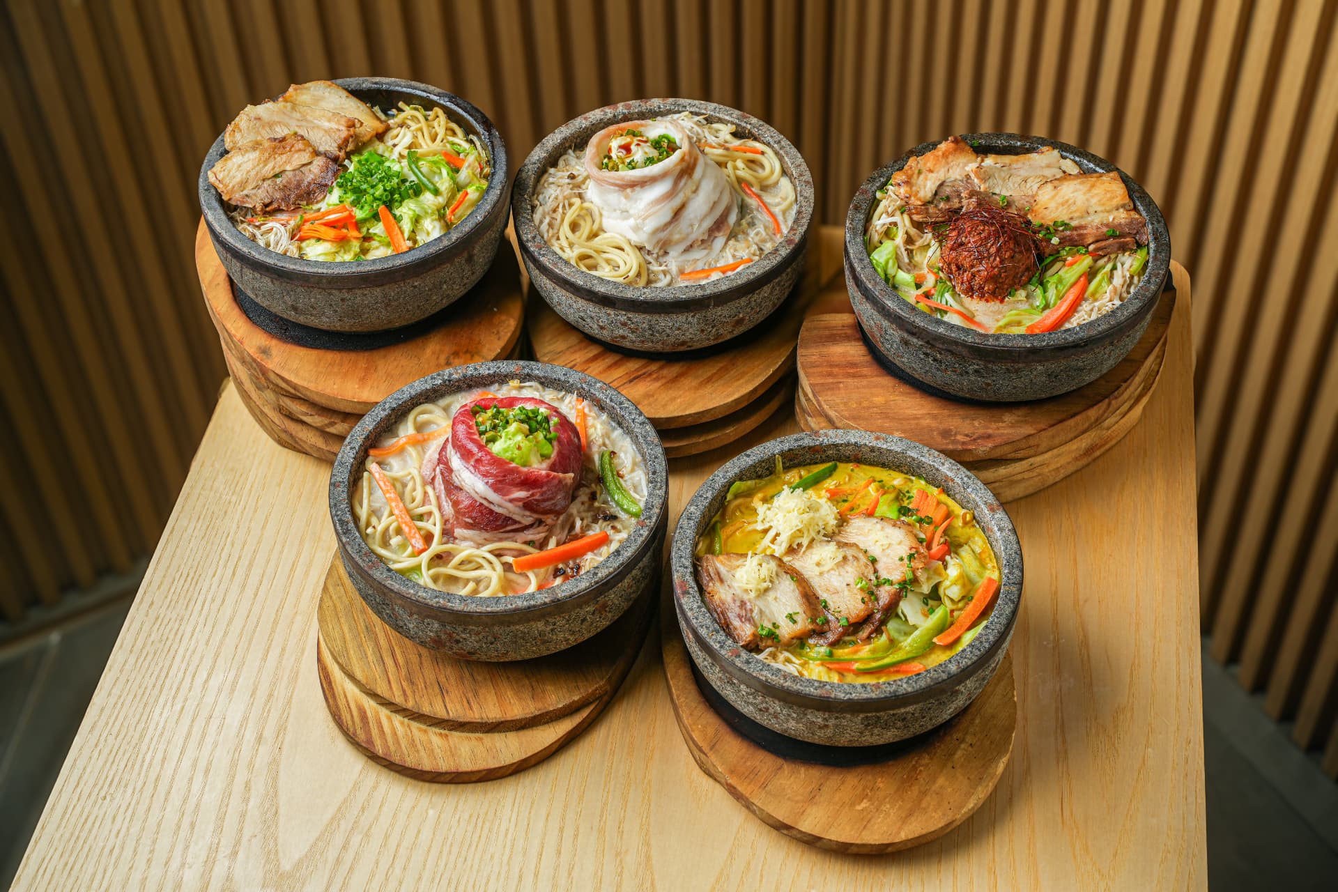 Five Kazan stone-bowl ramen dishes on wooden coasters